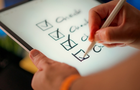 Main cochant des cases sur une checklist numérique avec un stylet, symbole de la norme ISO 9001 révisée