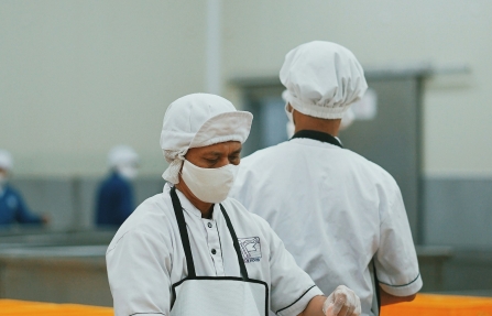 Chef en uniforme blanc découpant de la viande dans un environnement de transformation alimentaire professionnel